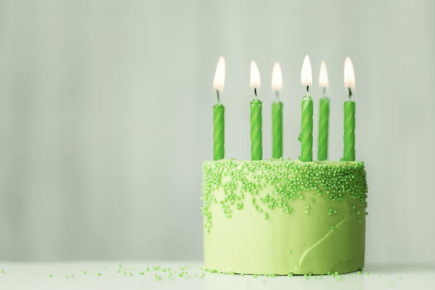 A green birthday cake with green sprinkles. There are 5 green, lit candles. 