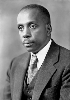 A black and white image of Howard Thurman. He is looking forward with a serious expression on his face, and he is wearing a gray suit, a white dress shirt, and a tie.
